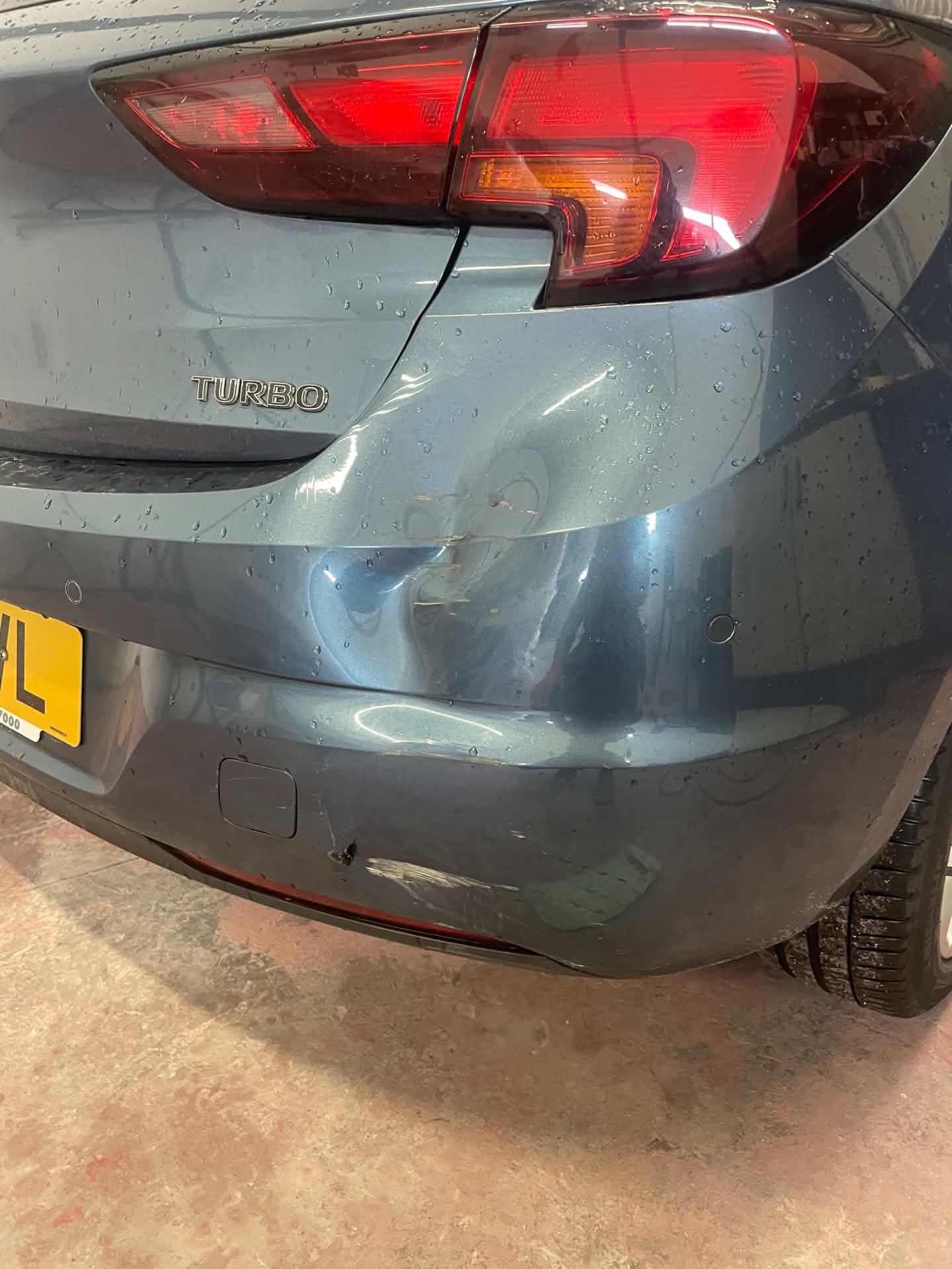 Car rear bumper before repair, showing a dent and cracked paint