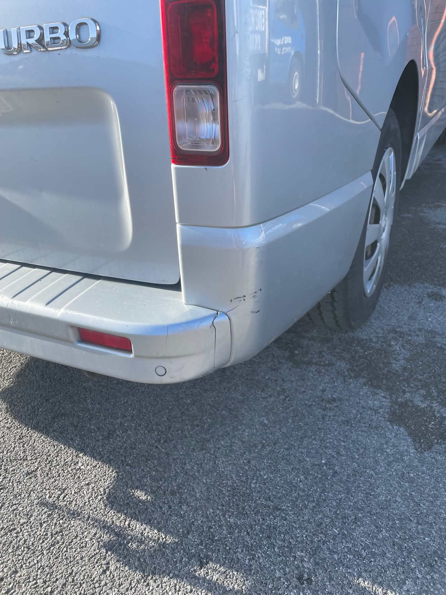 Silver van rear bumper before repair, close up of crack